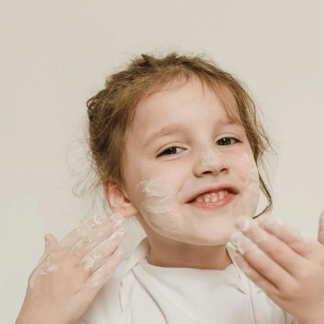 A smiling child with dabs of cream on her cheeks and hands