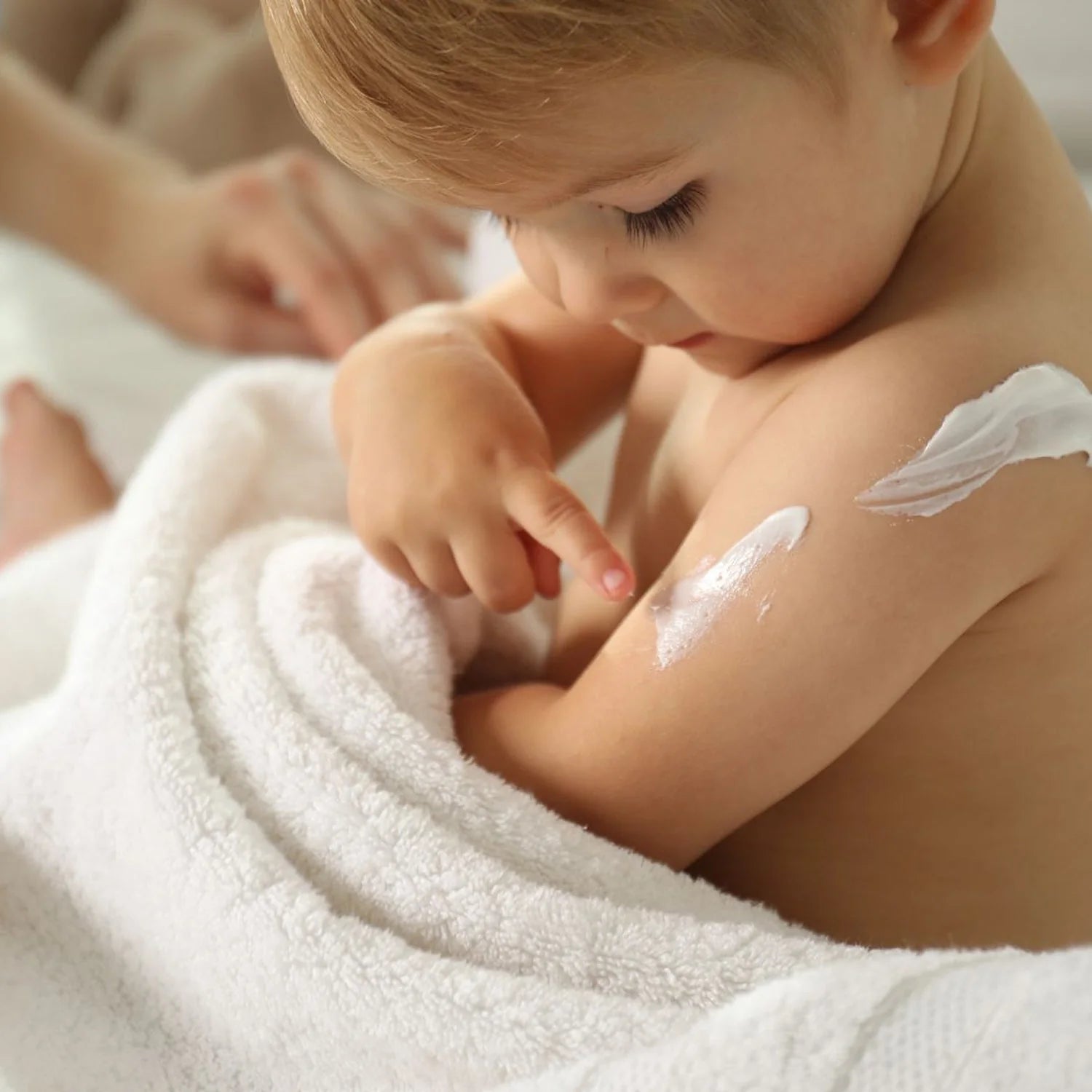 A toddler wrapped in a towel having cream applied to their arm
